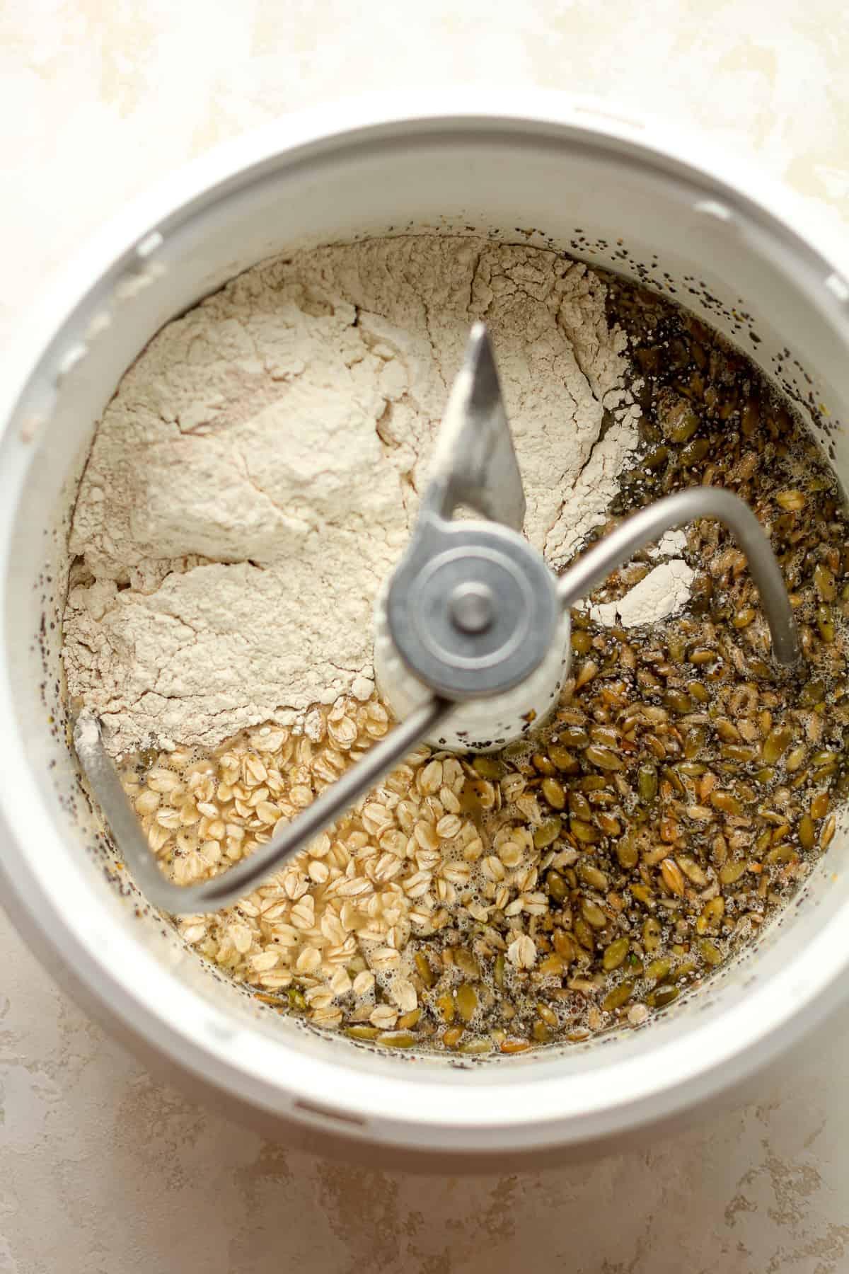 The mixer bowl with the ingredients showing the oatmeal, seeds, nuts, and flour.