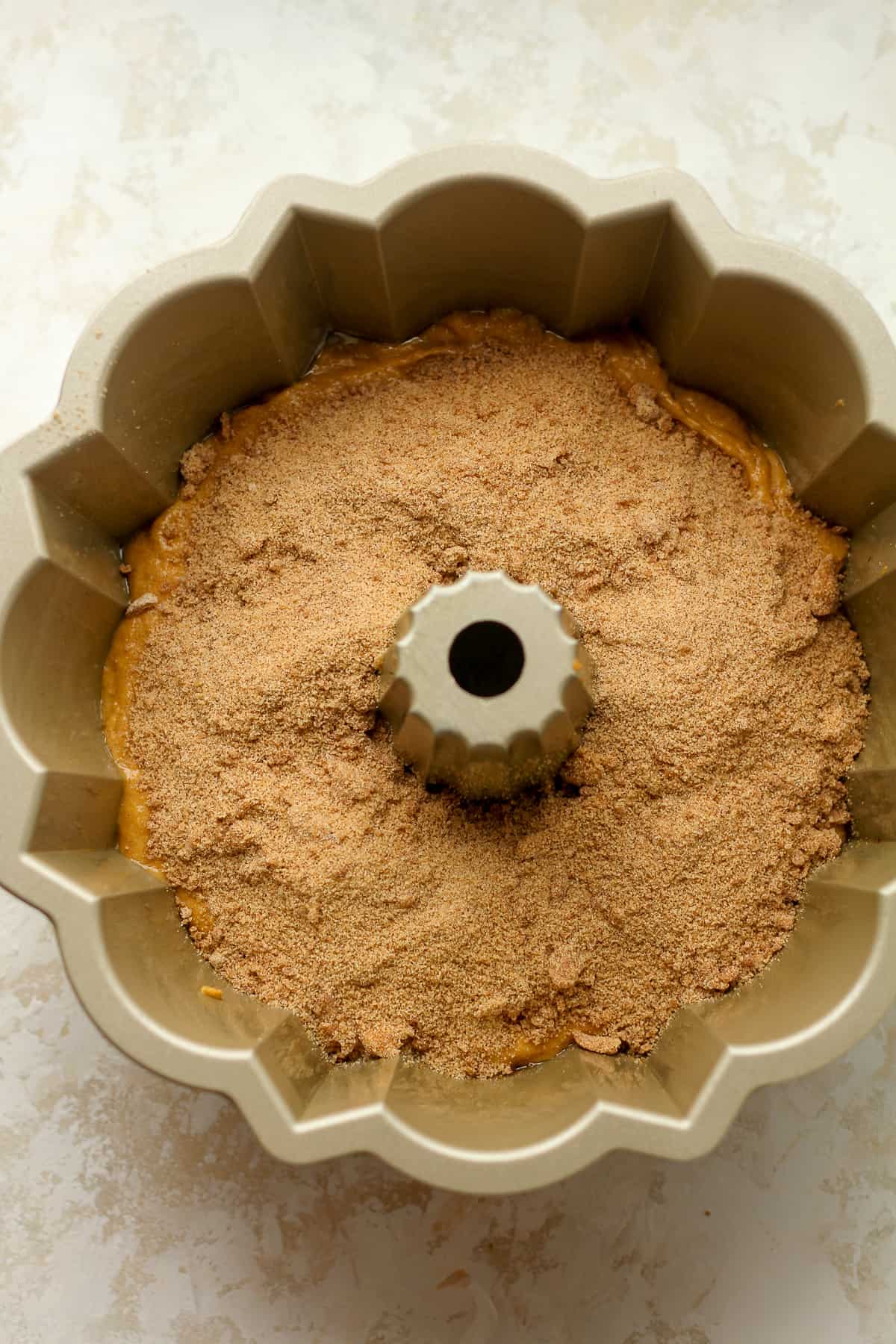A bundt pan with half of the batter plus the streusel layer on top.