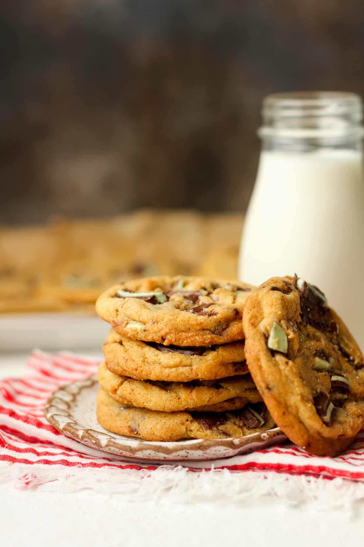 A side view of a plate of stacked mint cookies beside a jar of milk.