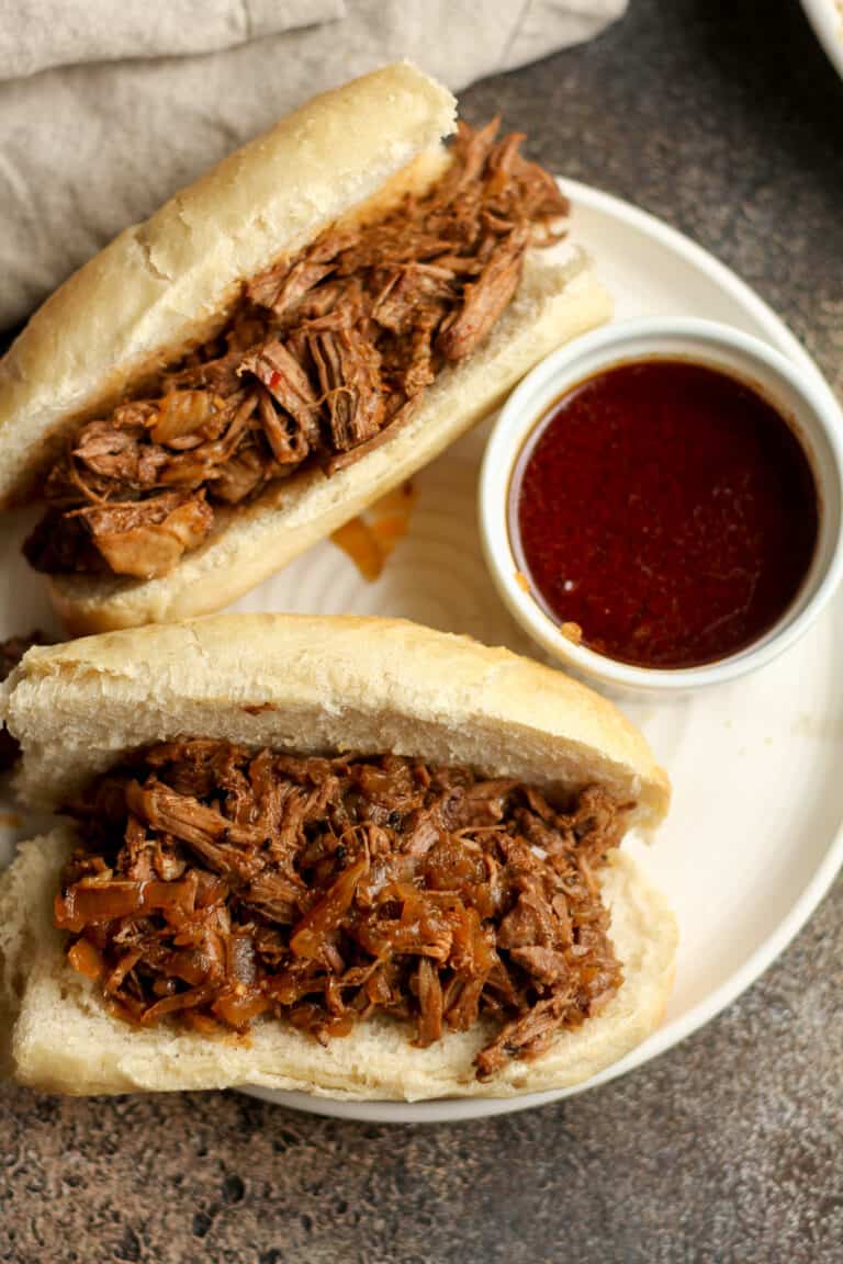 Overhead view of two beef au jus sandwiches with au jus on the side.