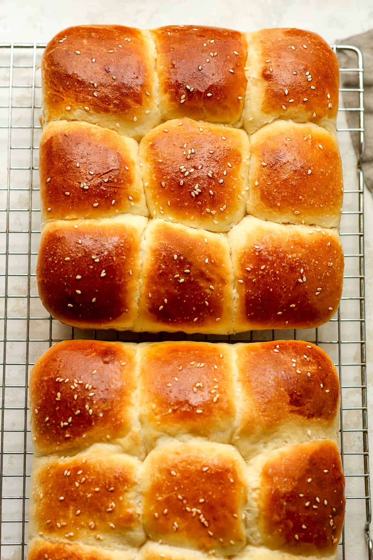 Two pans of dinner rolls on a cooling rack.
