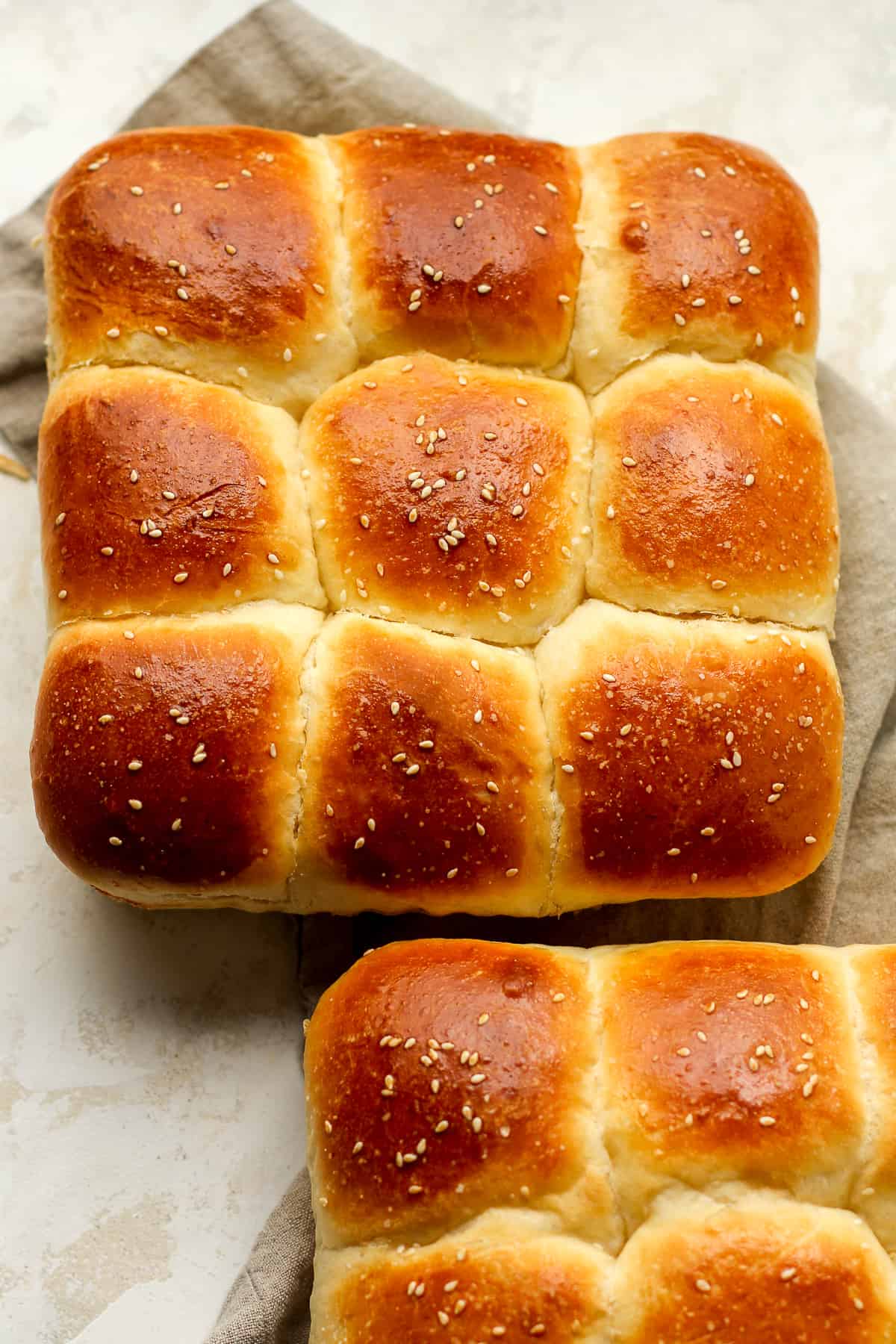 Two pans of brioche dinner rolls on a gray napkin.