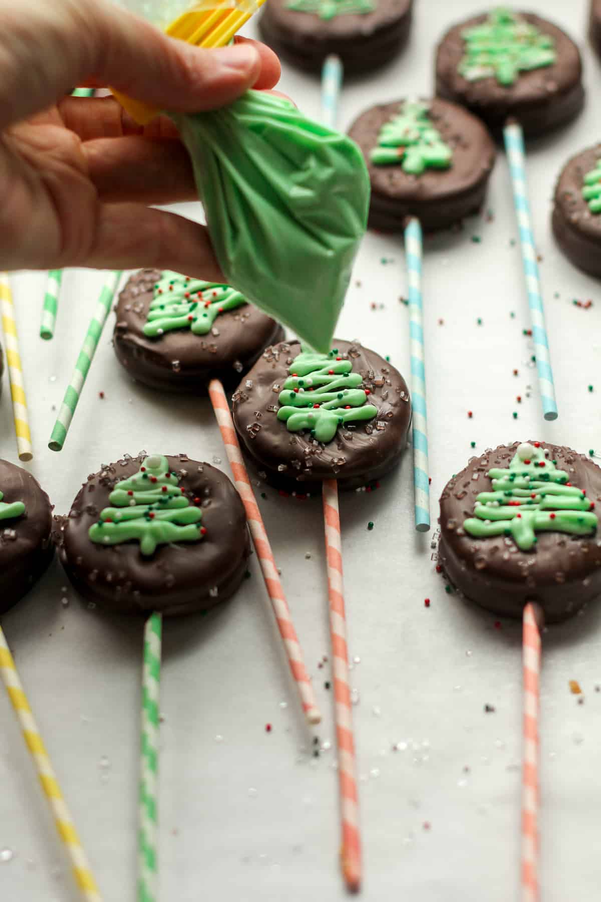 A sheet pan of the ritz pops with my hand holding the green decorating chocolate in a bag.