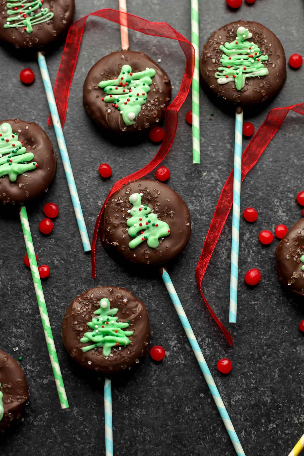 A black background with some chocolate covered ritz cracker pops with red hots.