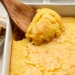 A creamy corn casserole with a wooden spoon scooping.