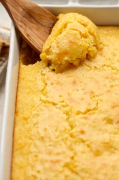 Side view of a dish of corn casserole with a wooden spoon scooping.