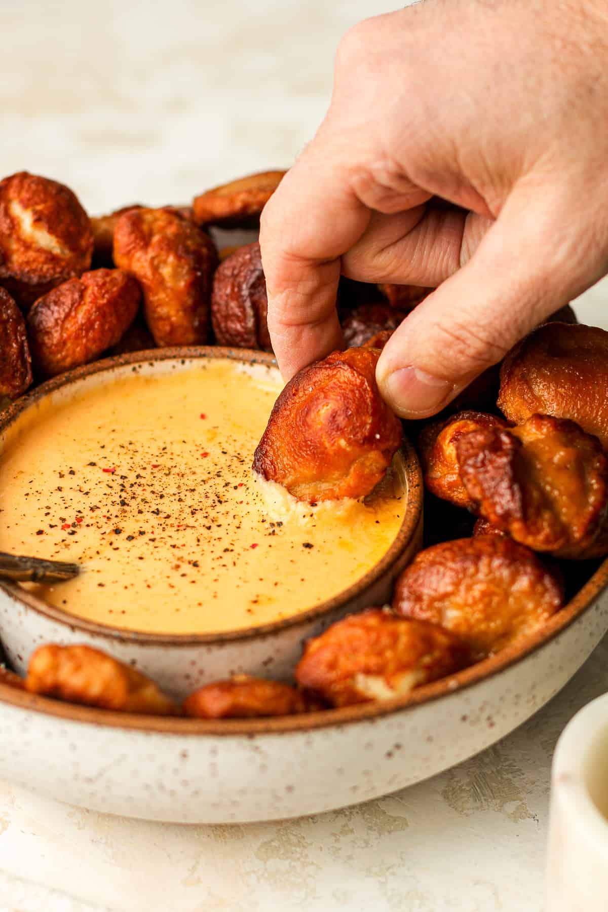 A hand dipping a pretzel bite into a bowl of homemade cheese dip.