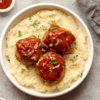 A bowl of the mashed potatoes topped with turkey meatloaf muffins.