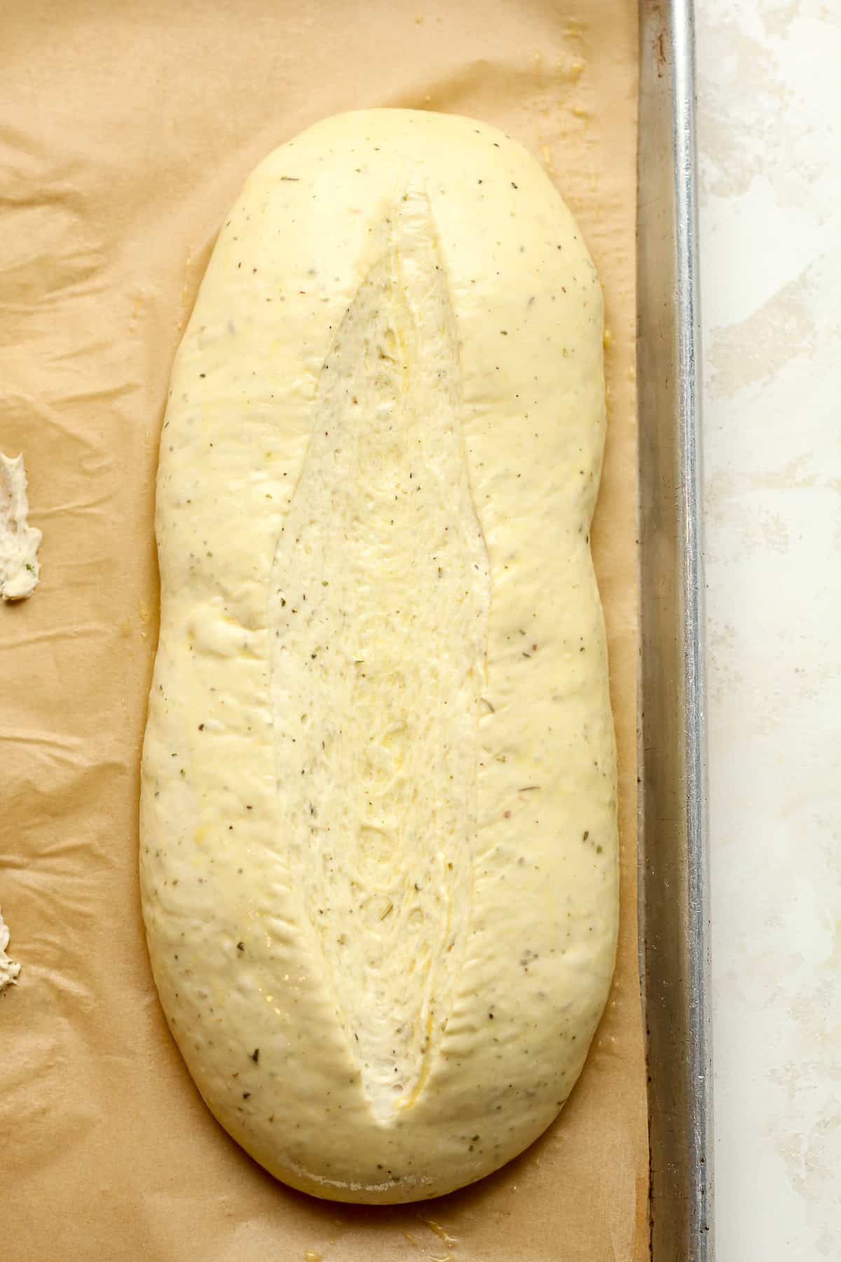 A loaf of Italian herb dough on a baking sheet.