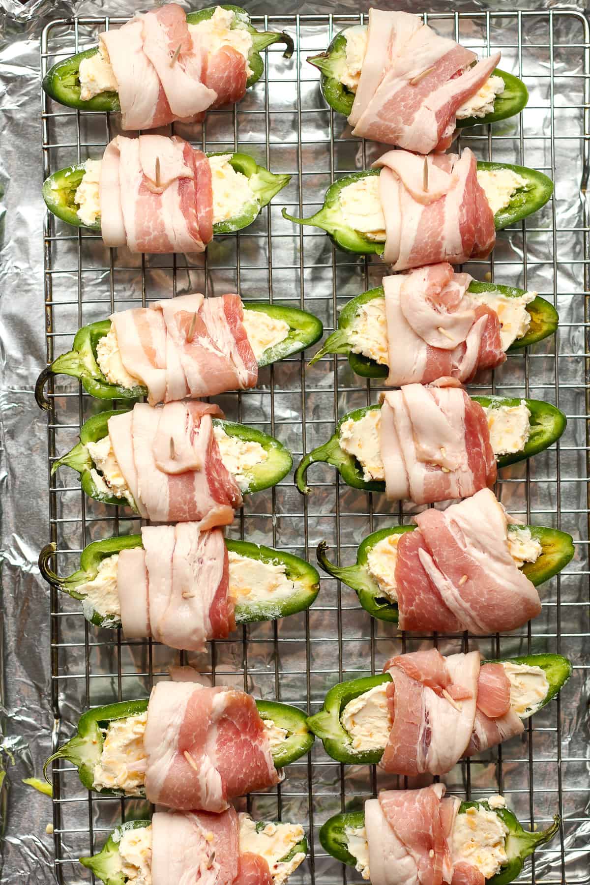 A wire rack of the raw bacon wrapped around stuffed jalapeños.
