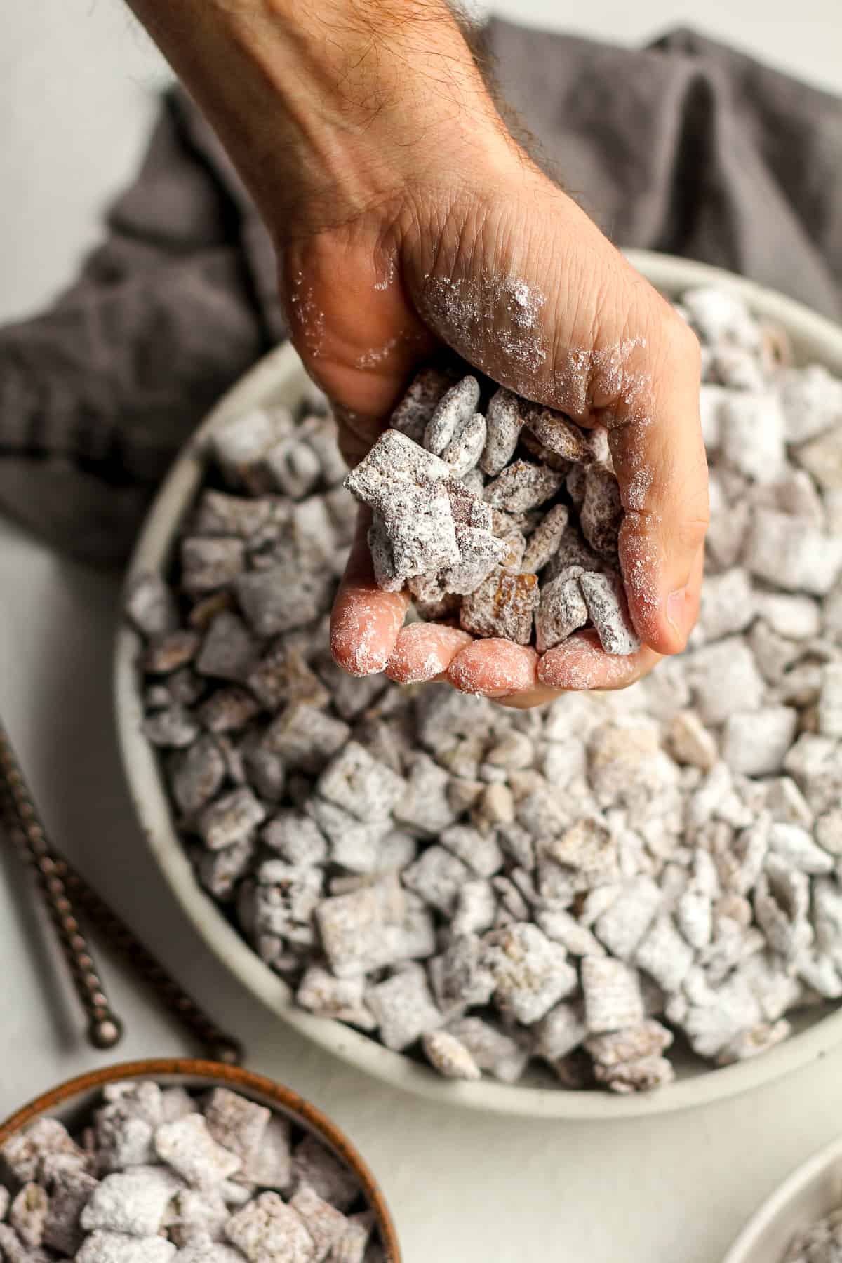 A handful of chocolate muddy buddies over top of a large bowl.