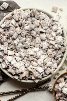 A large bowl of chocolate muddy buddies with some spilled out.