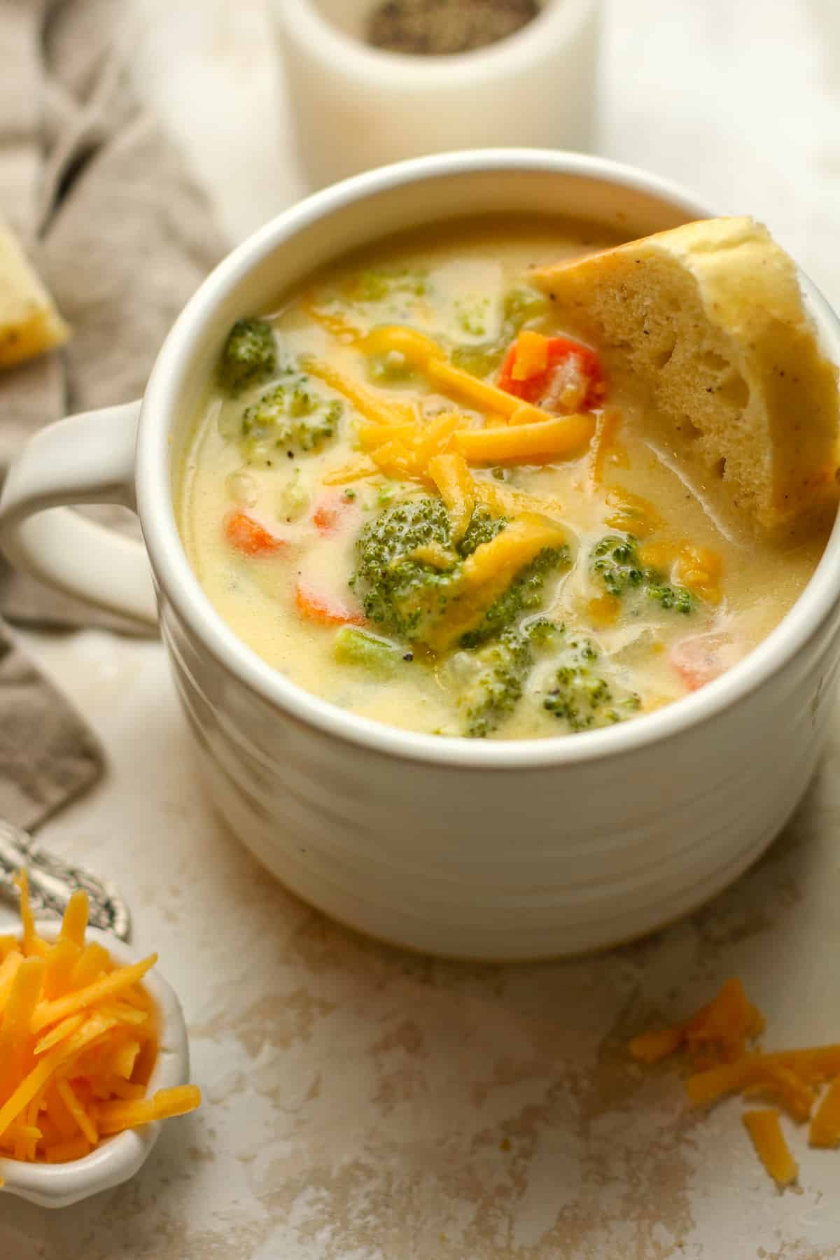 A large mug of cheddar broccoli soup with shredded cheese on top.