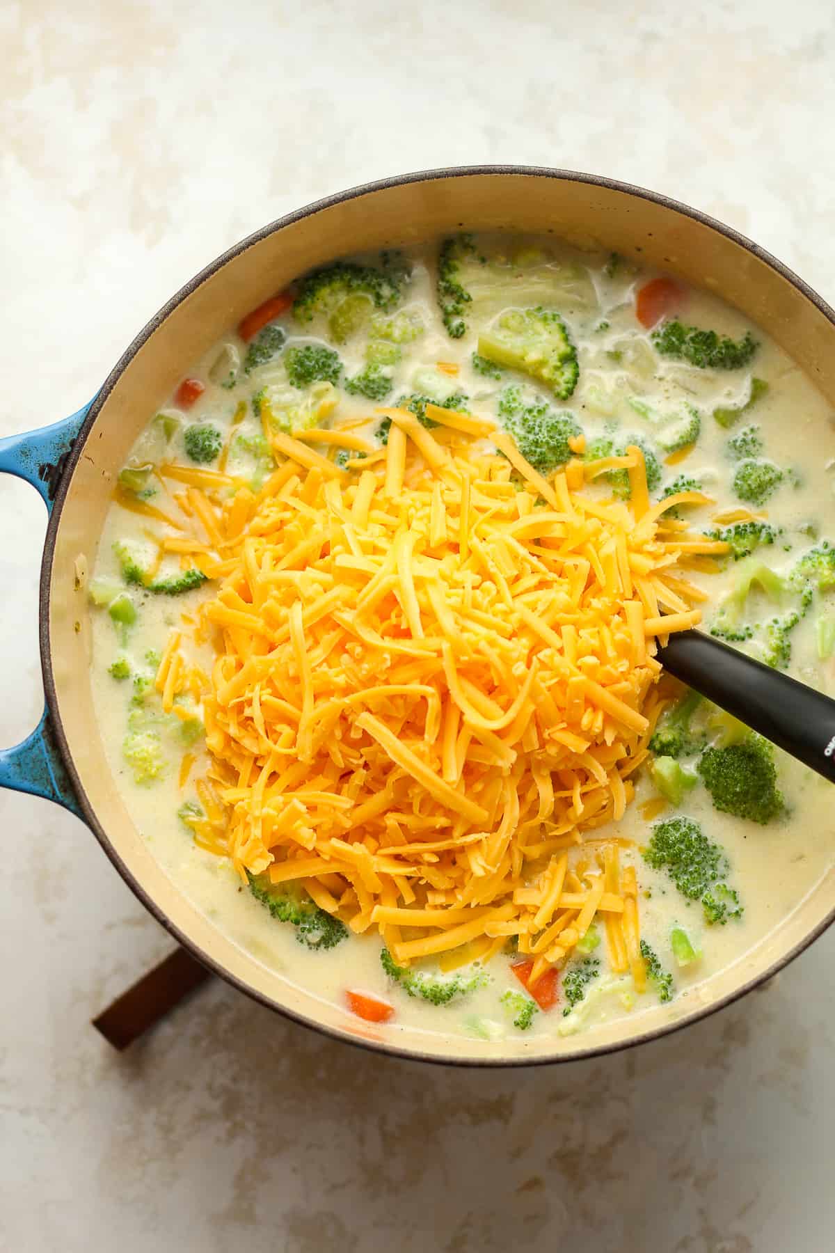 A pot of broccoli soup with shredded cheddar on top.