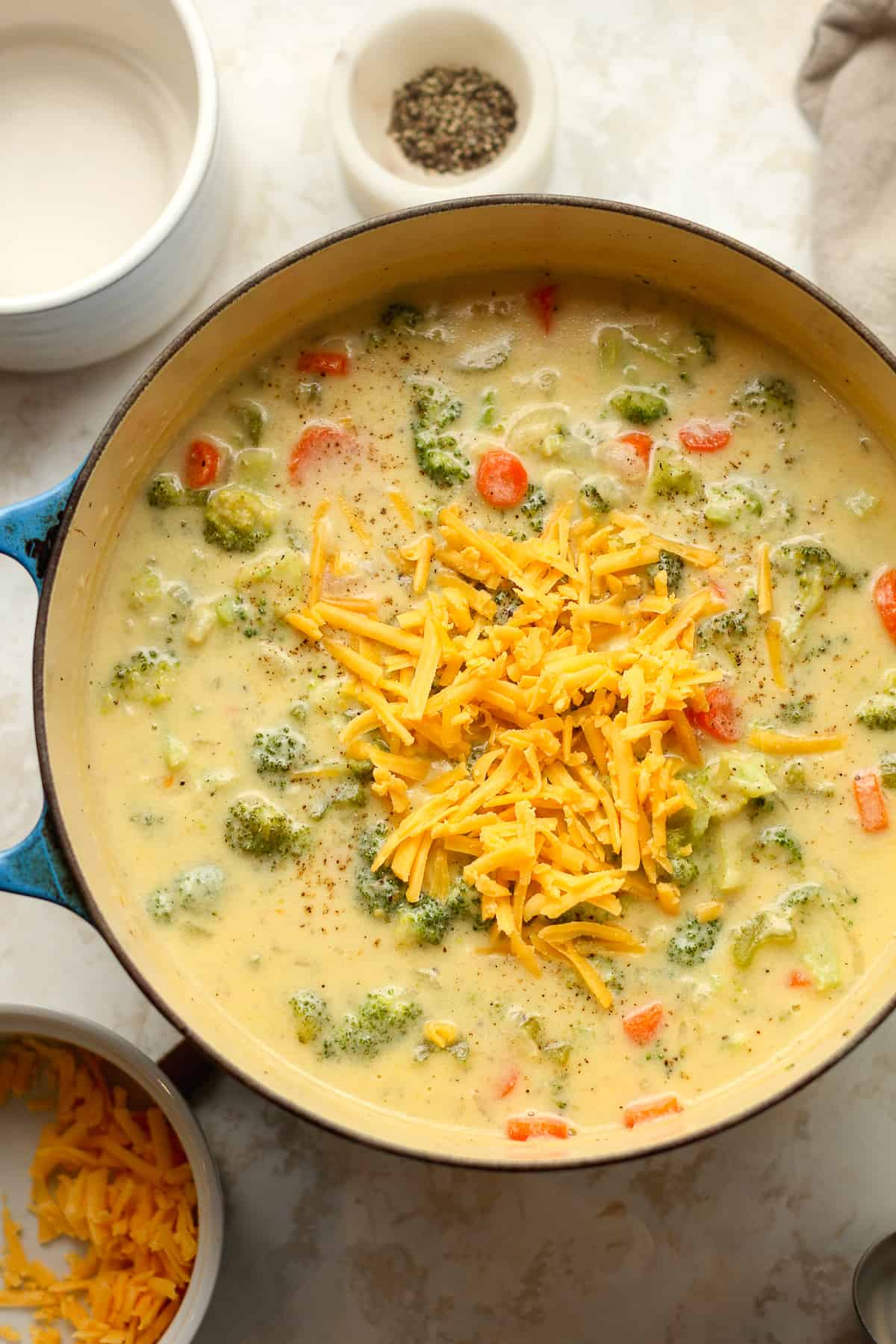 A stock pot full of creamy broccoli cheddar soup with cheese on top.