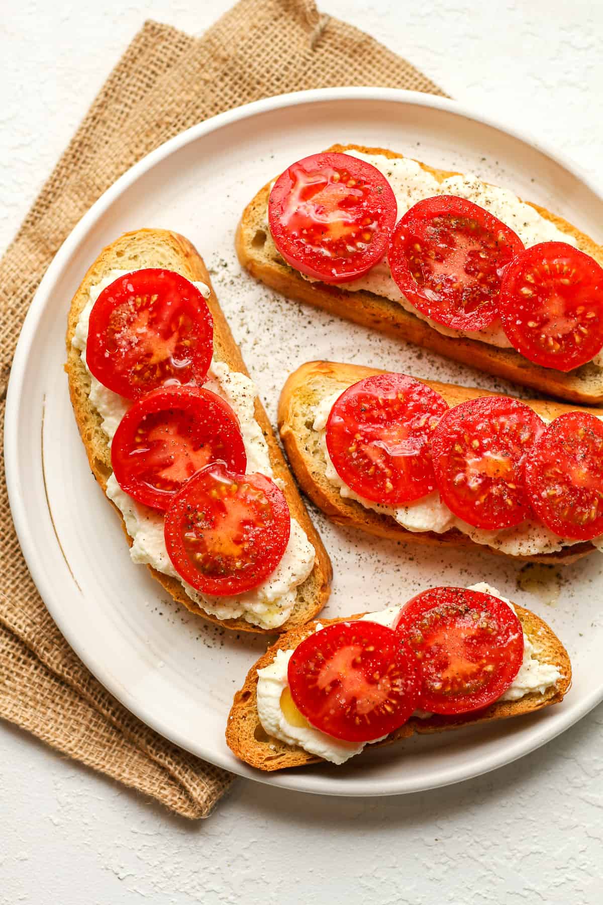 A plate of crostini using sliced Italian bread - topped with ricotta cheese and tomatoes.