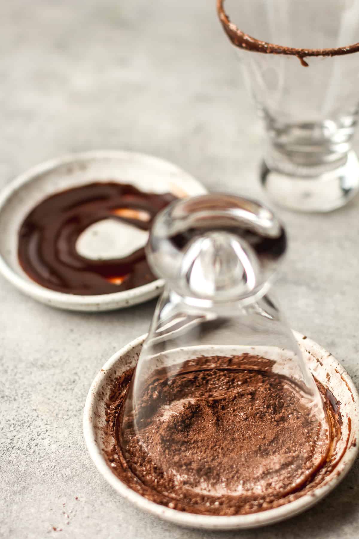 Side view of two glasses, one dipping in a plate of the chocolate.