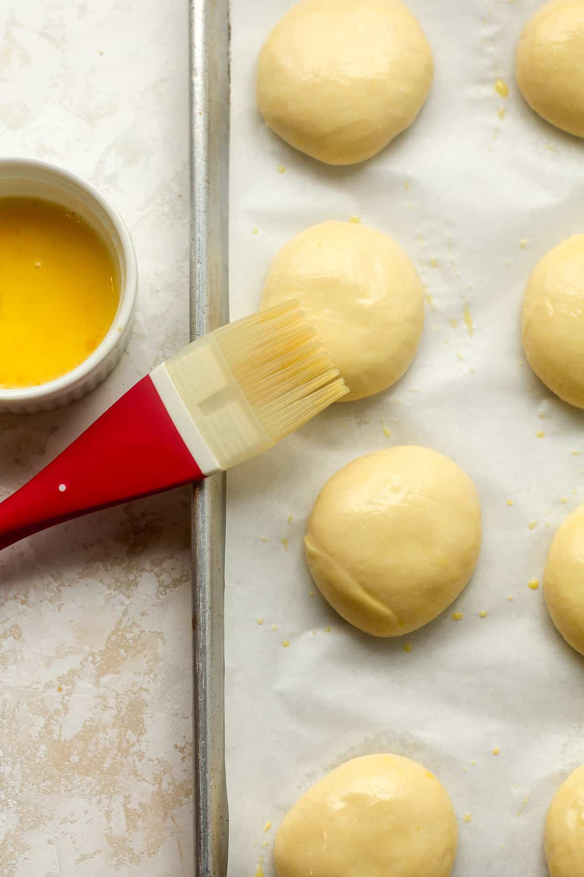 A brush beside the egg wash and the brioche dough buns.