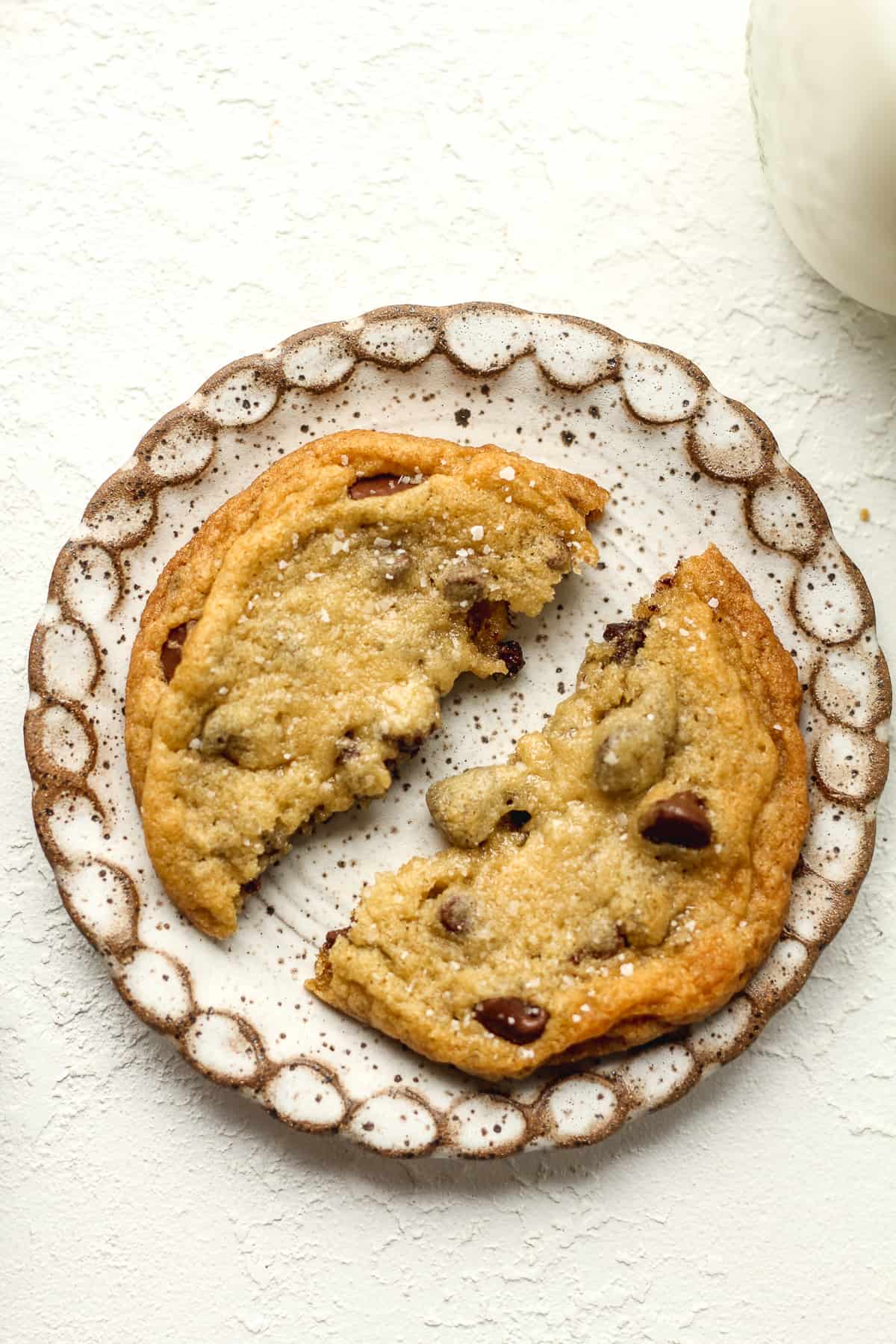 A small plate of a halved chocolate chip cookie with a glass of milk.