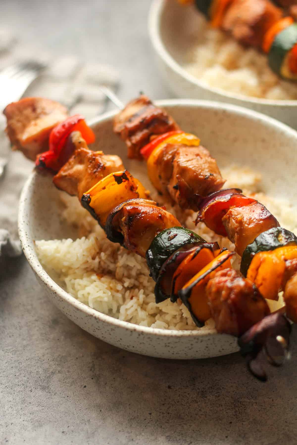 Side view of a bowl of rice with two chicken skewers on top.