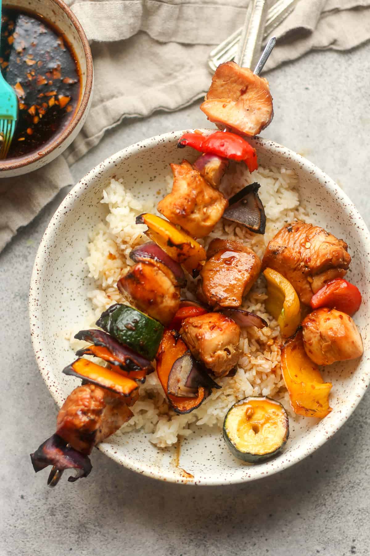 Overhead view of a bowl with rice and two skewers with some Asian marinade.