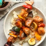 A bowl of grilled Asian chicken skewers over rice with a gray napkin.