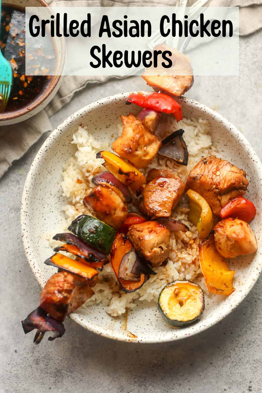 A bowl of grilled Asian chicken skewers over rice with a gray napkin.