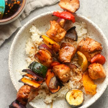 A bowl of rice topped with Asian chicken skewers.