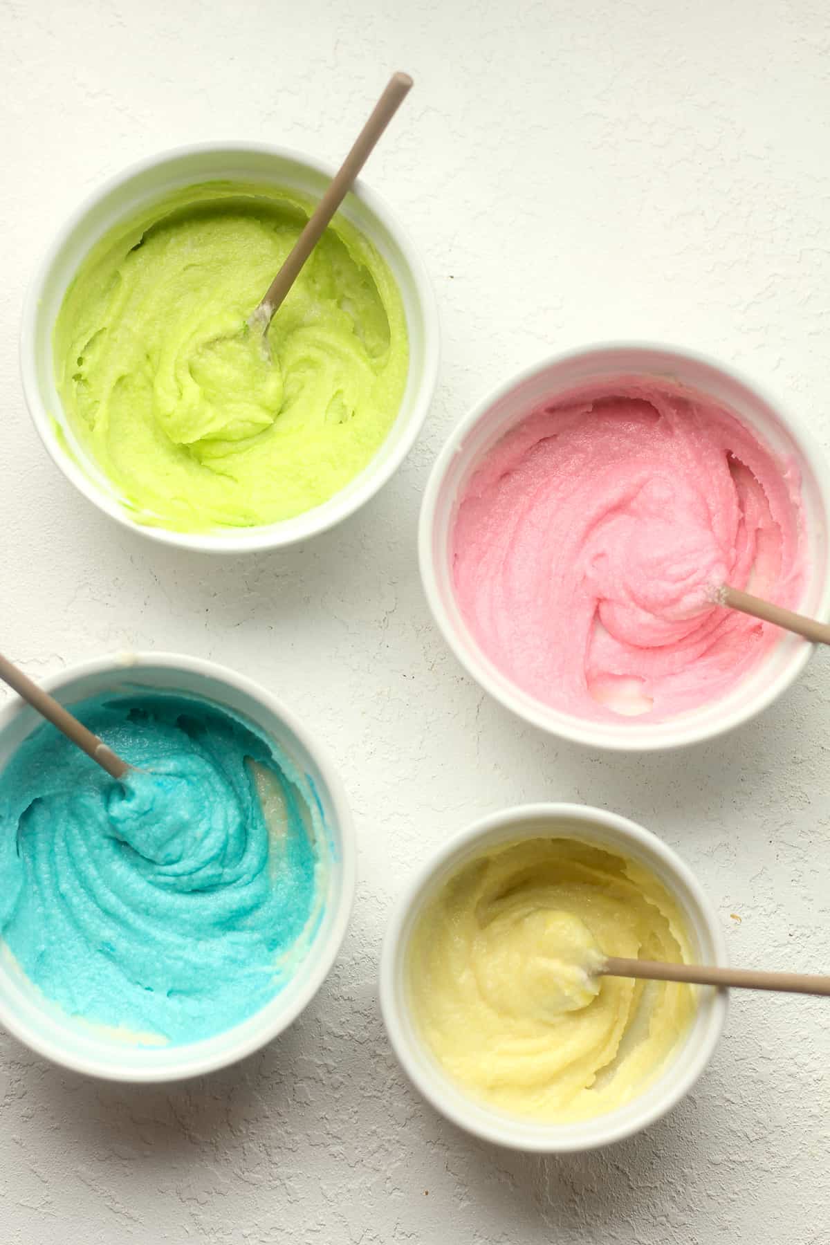 Four small bowls of colorful buttercream.