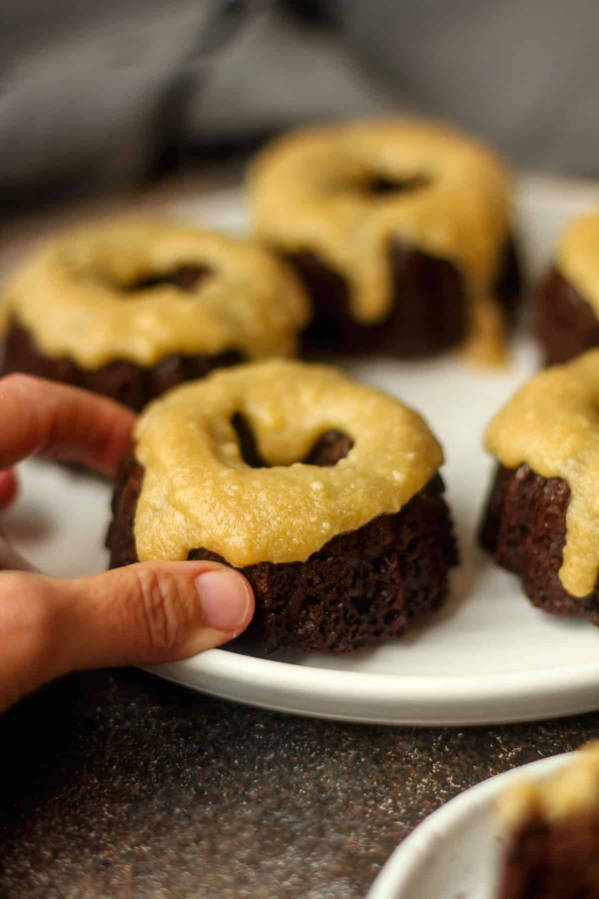 My hand grabbing a mini chocolate bundt cake from a plate.