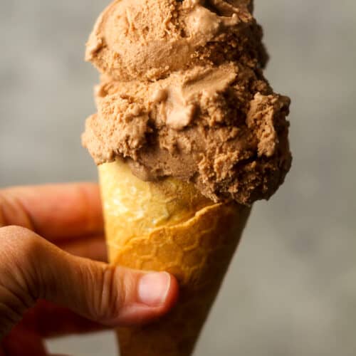 Side view of a hand holding an ice cream cone with nutella ice cream.