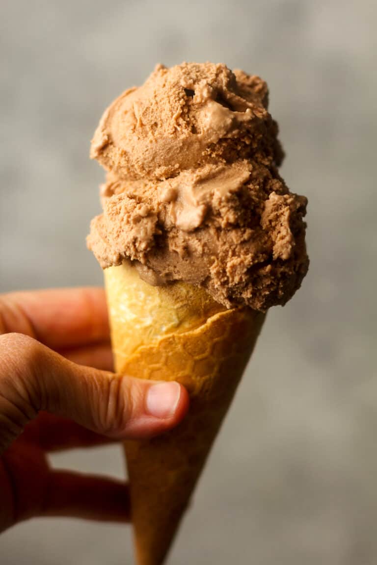 Side view of a hand holding an ice cream cone with nutella ice cream.