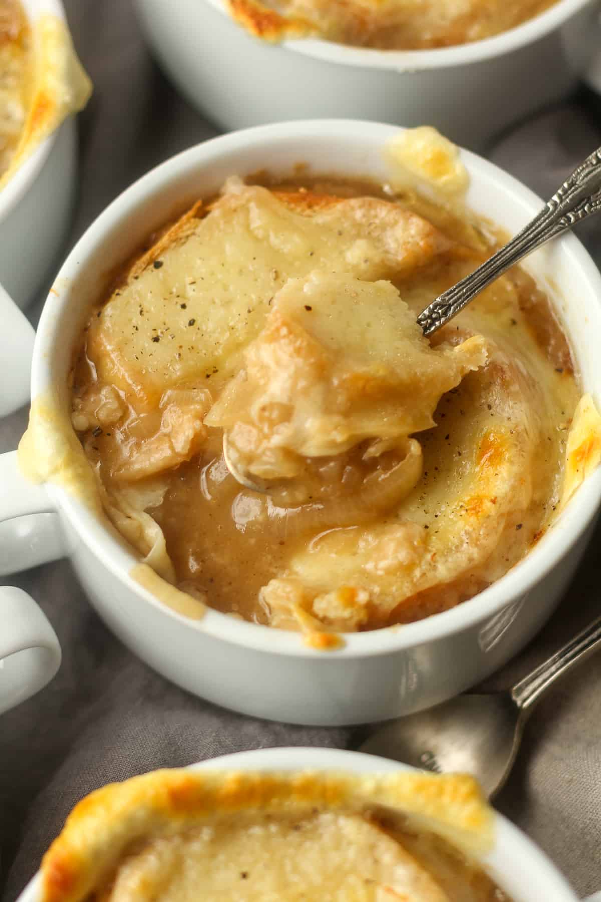 Side view of mugs of French Onion Soup, one showing a large bite out.