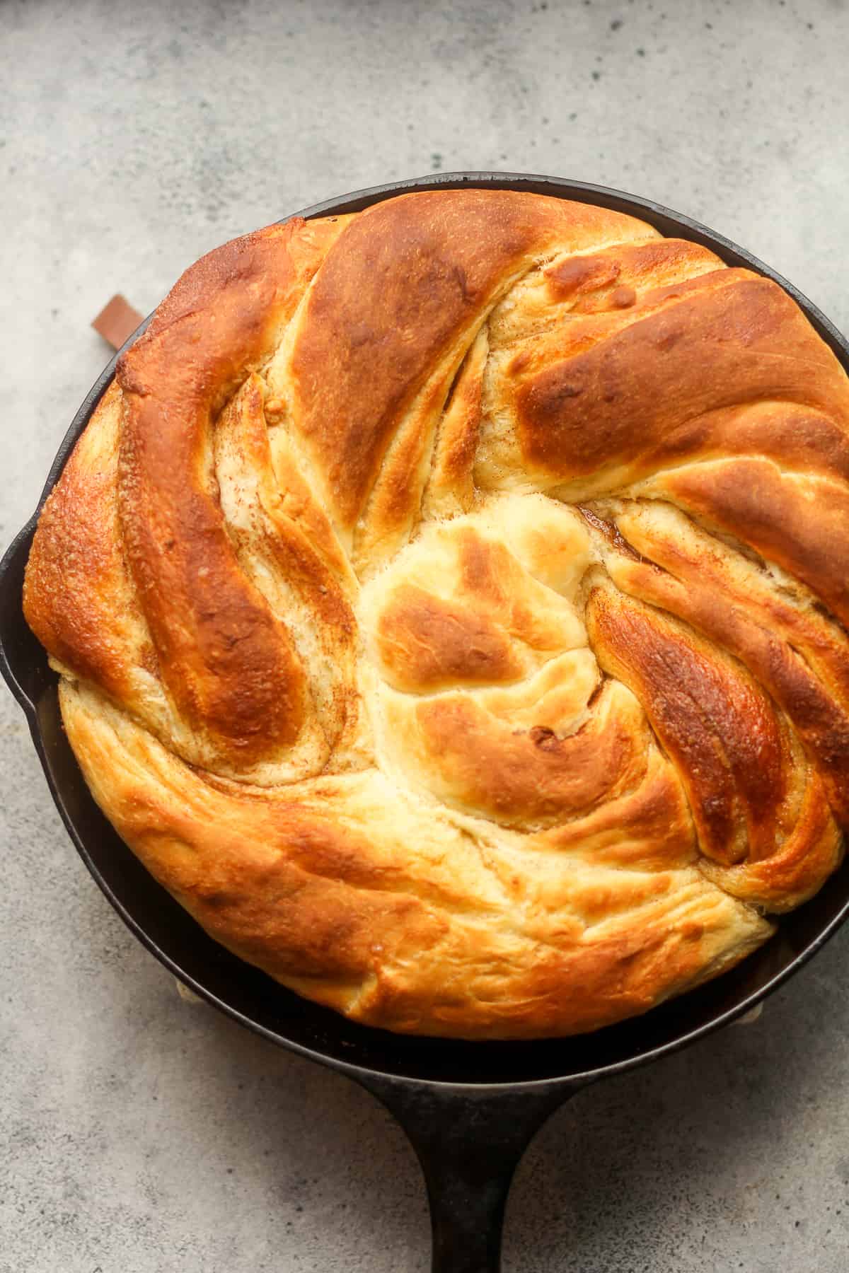 A cast iron skillet with a just baked cinnamon twist roll.