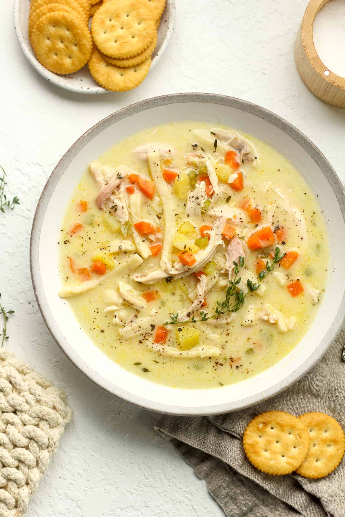 A bowl of creamy chicken noodle soup with a plate of crackers.