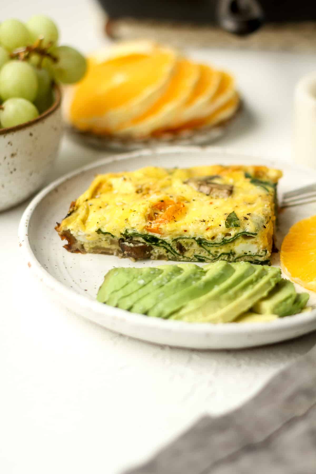 Side view of a plate with a frittata with some sliced avocado and some fruit.