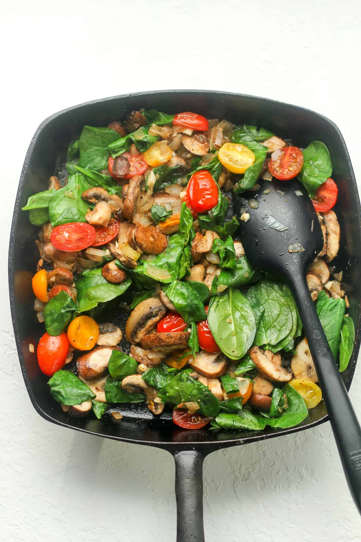 A square cast iron pan with sautéed veggies.