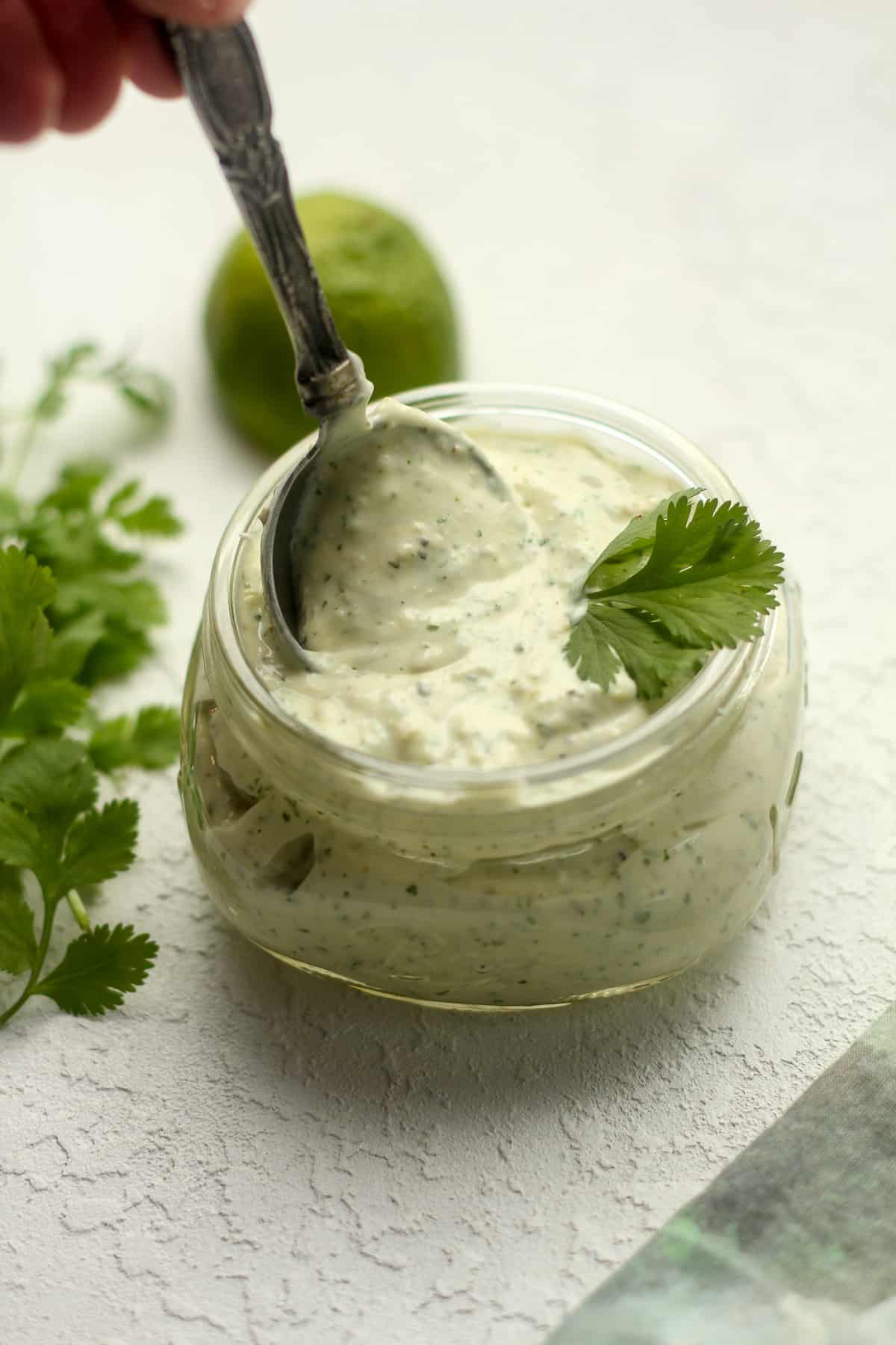 Side view of a jar of jalapeno ranch dressing with a tablespoon being lifted out.