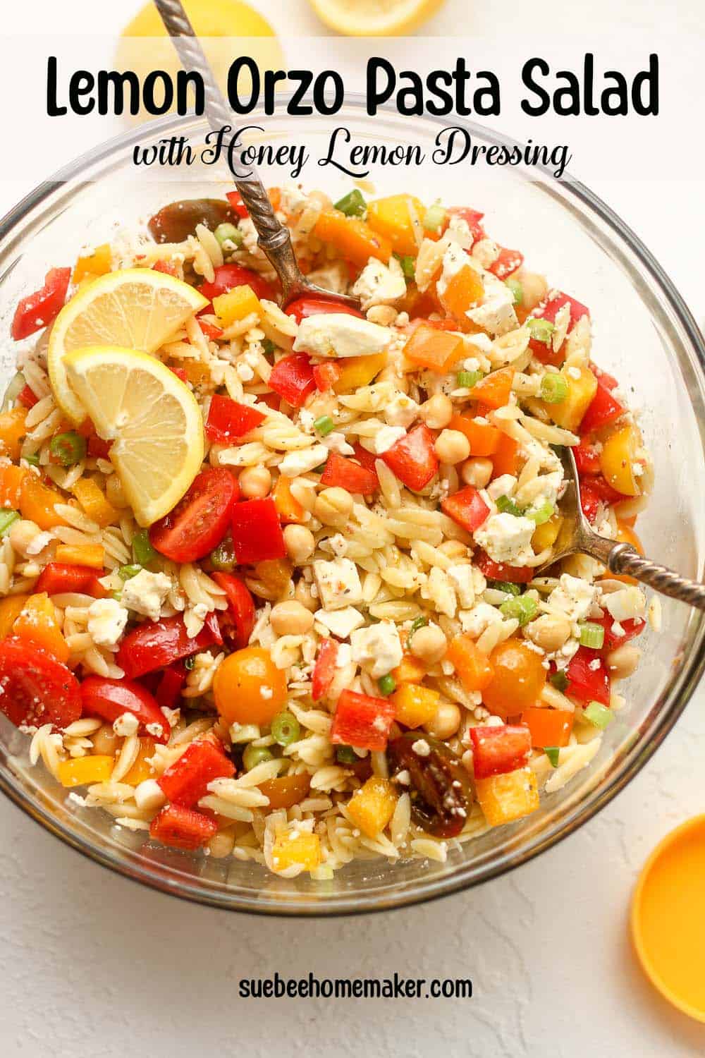 A large glass bowl of lemon orzo pasta salad with serving spoons.