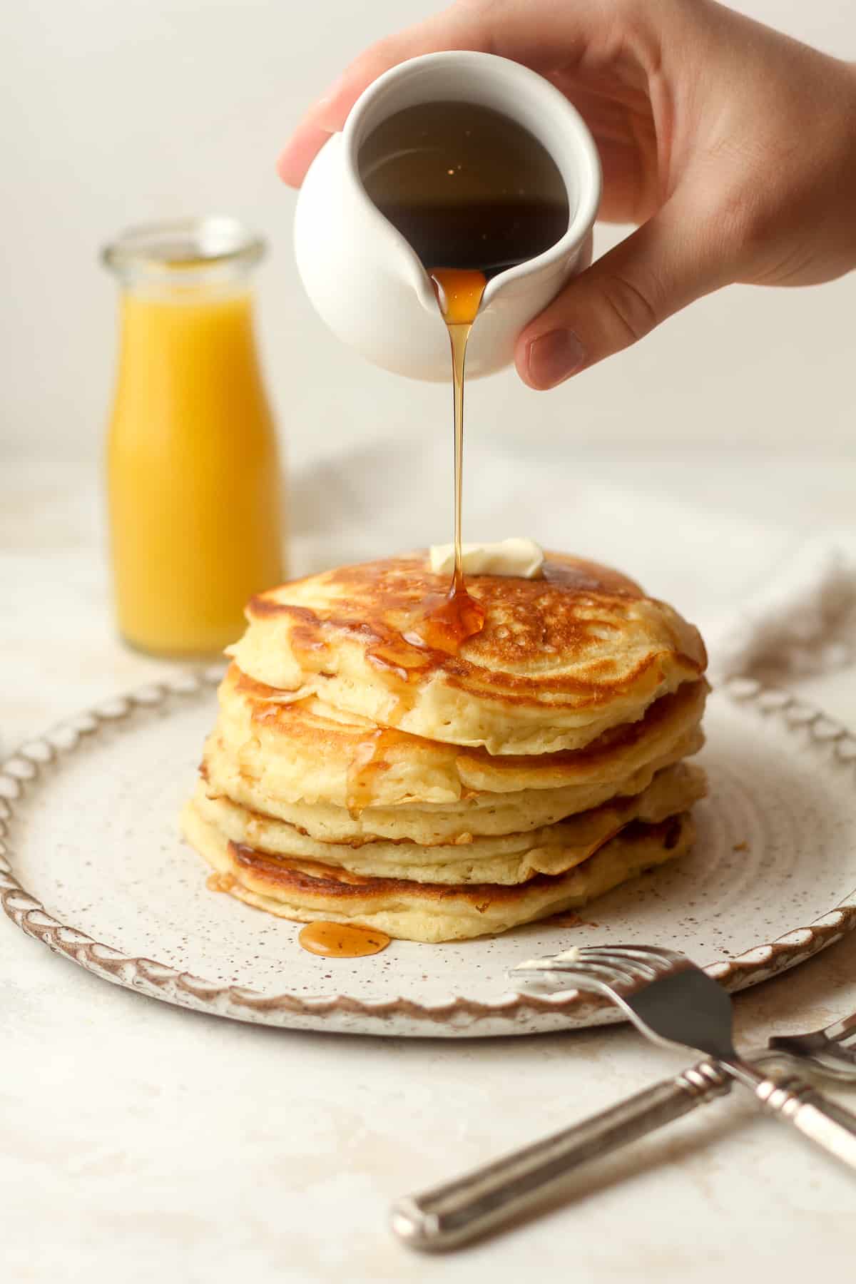 A hand pouring syrup over a stack of buttermilk pancakes.
