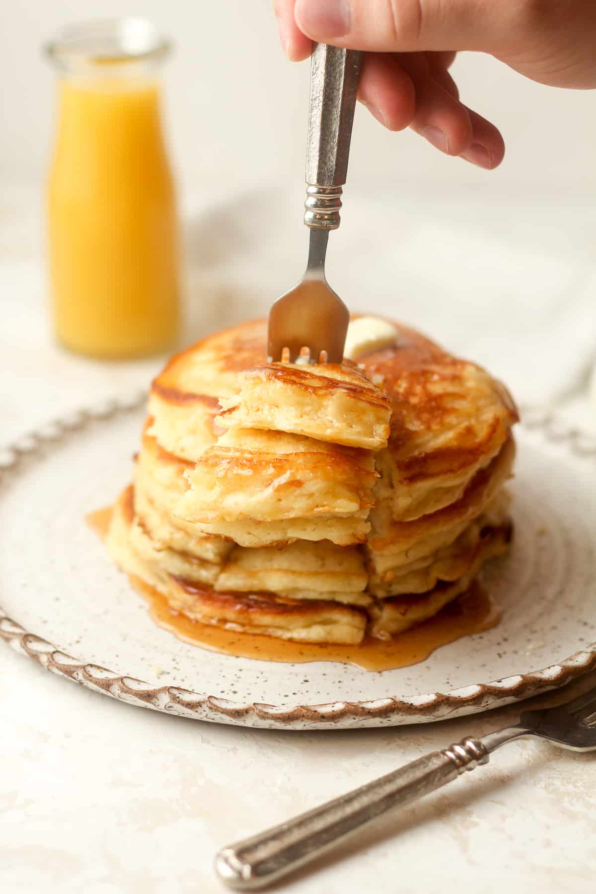 A hand sticking a fork in a stack of pancakes.