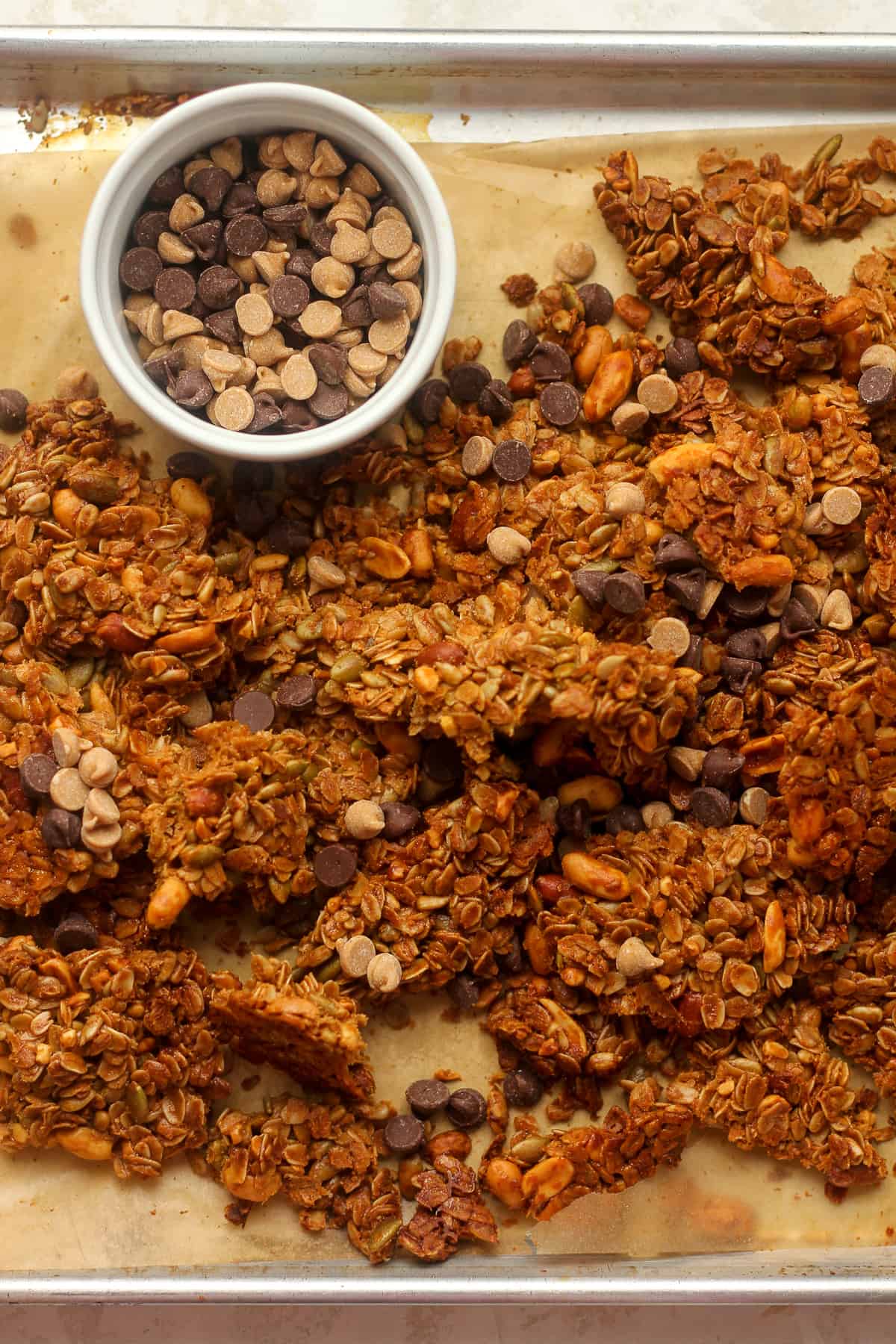 Overhead view of the granola clusters on a baking sheet with a small bowl of chips.