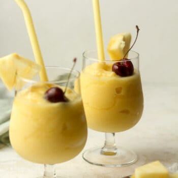 Side view of two frozen Pina coladas with cherries.