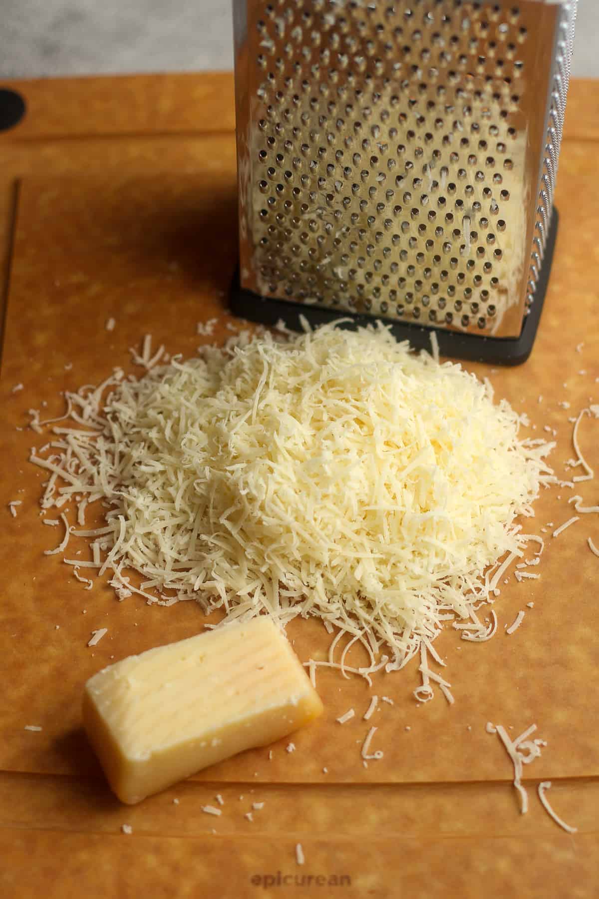 A board with a box cutter and some shredded parmesan cheese.