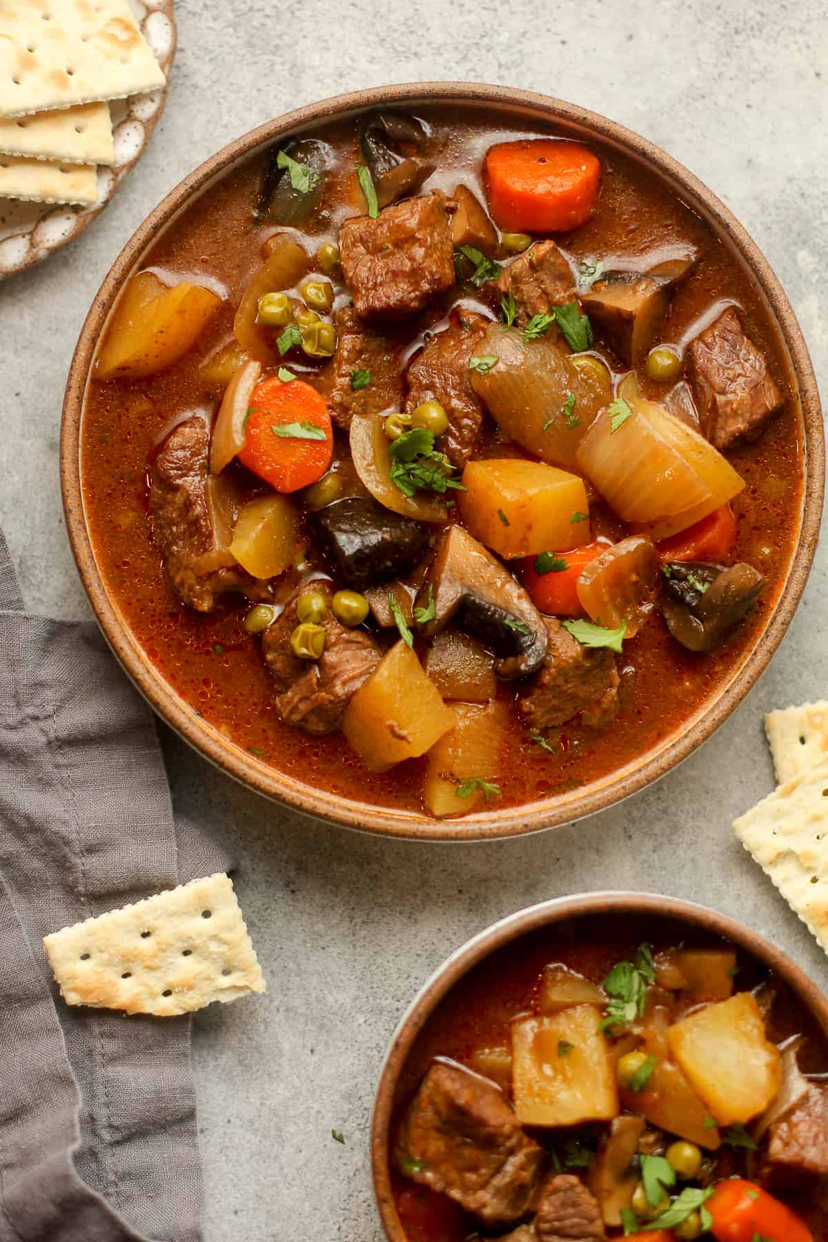 Two bowls of beef stew with crackers.
