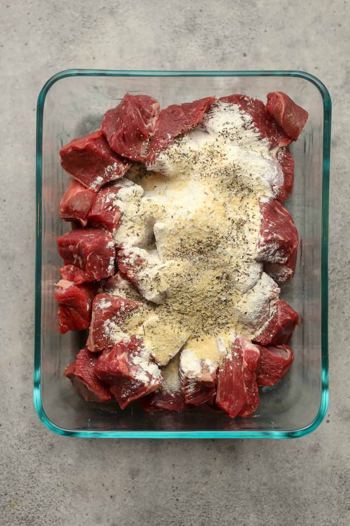 A bowl of the beef pieces with flour and seasonings.