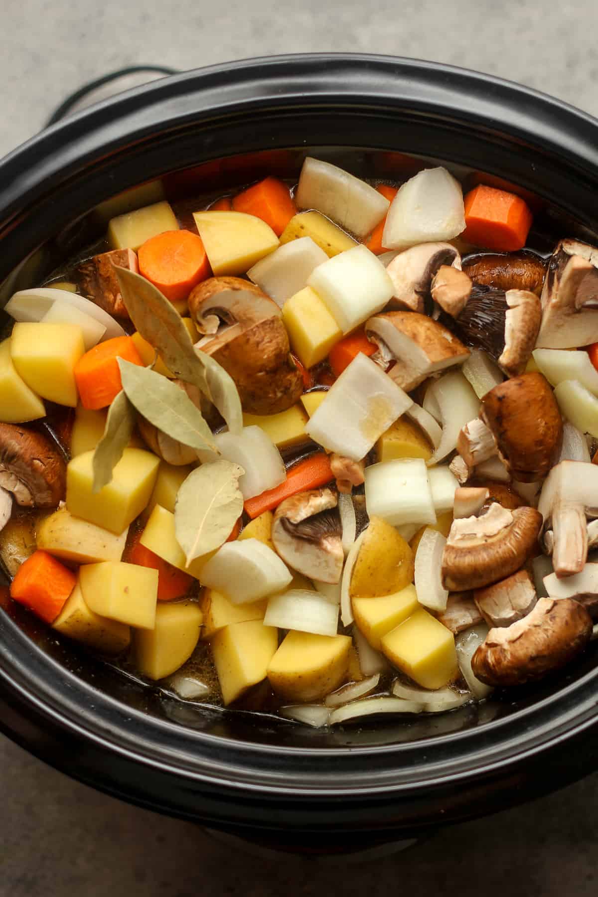 A black slow cooker topped with veggies.