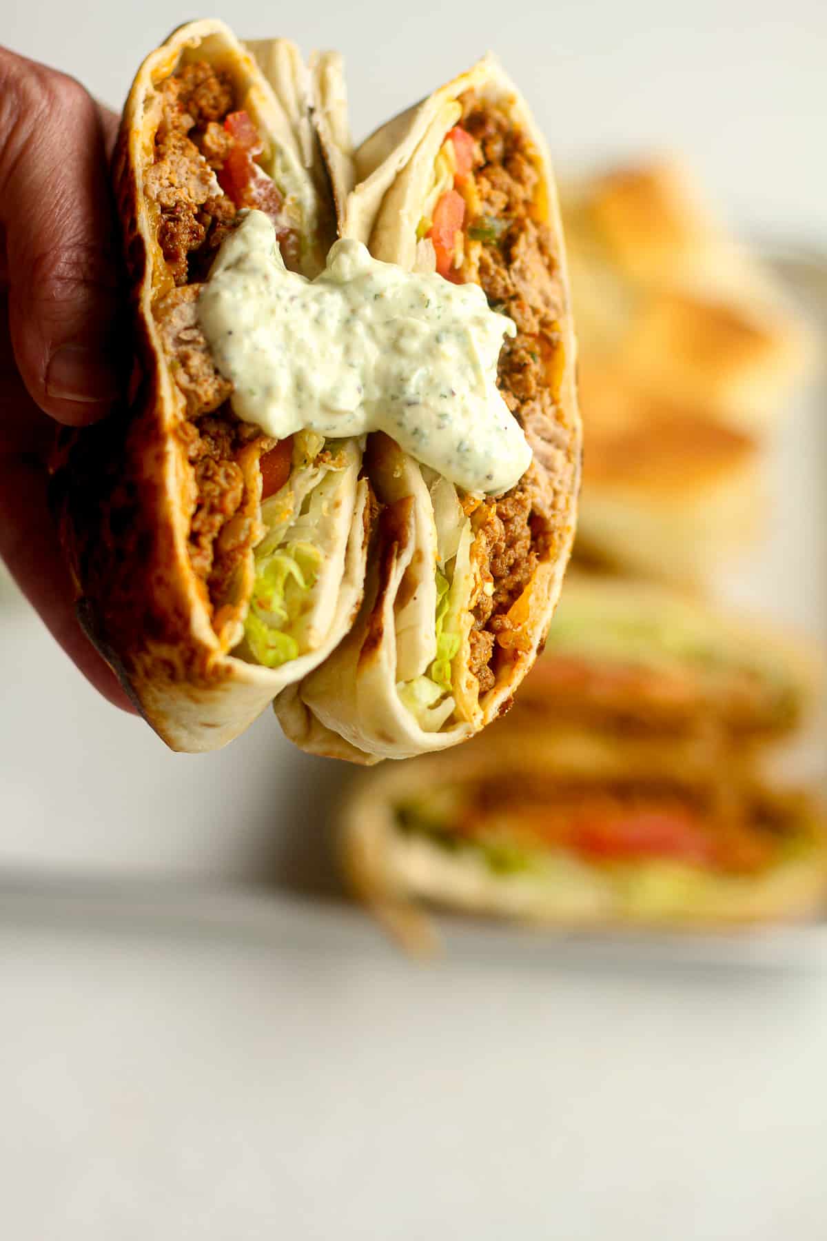 A hand holding a split taco crunch wrap with jalapeno ranch.