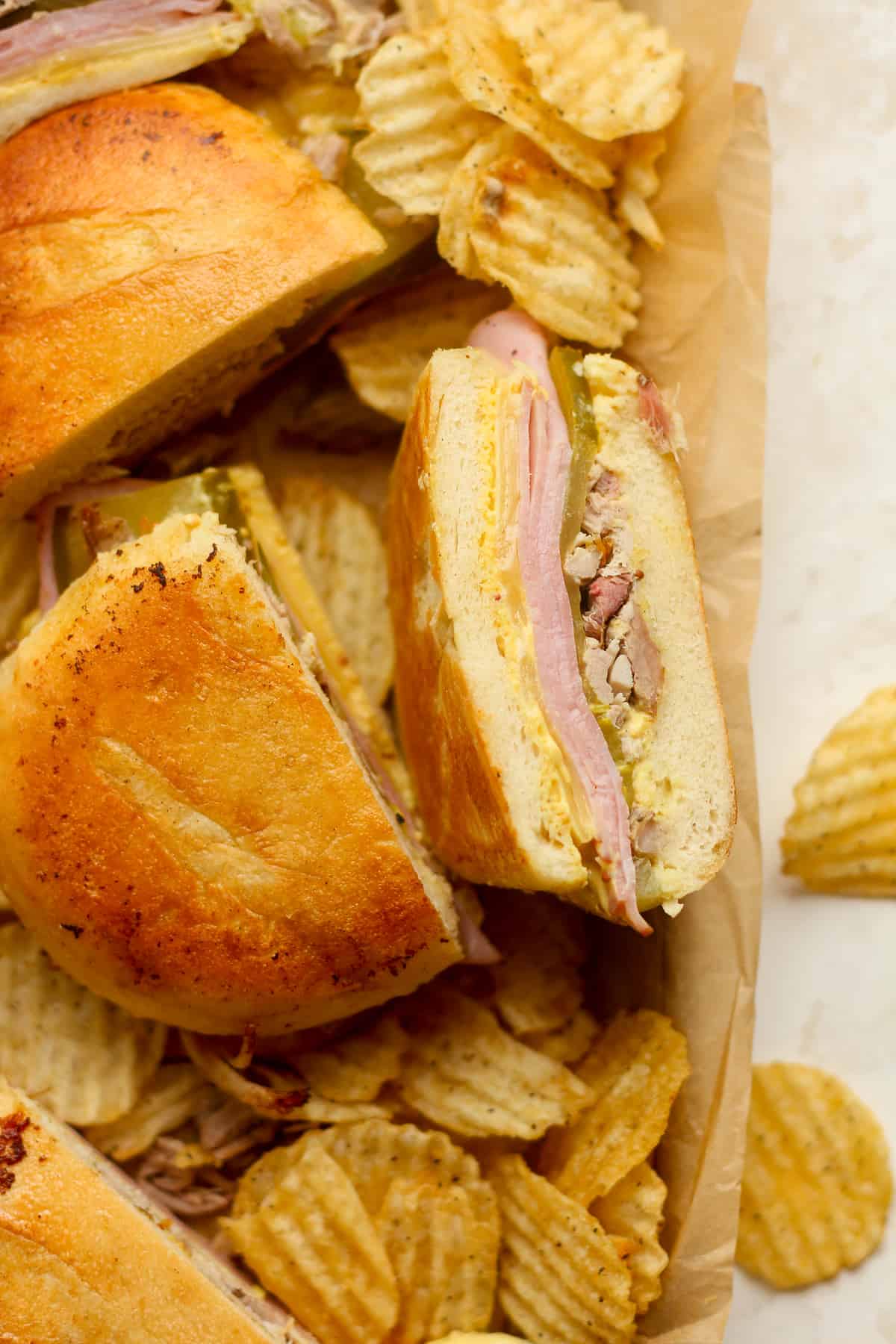 A pan of halved Cuban sandwiches with some chips.
