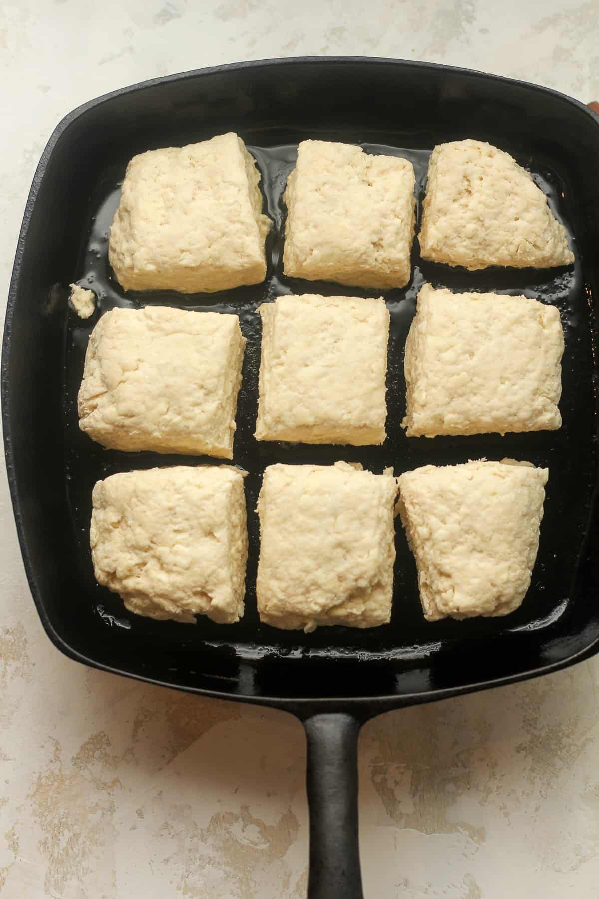 A square skillet of biscuit dough in squares.